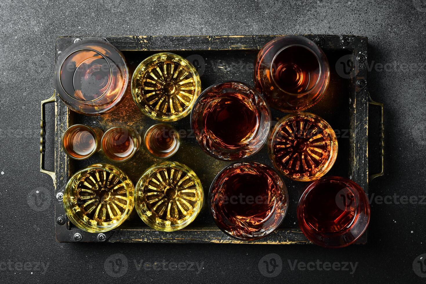 Wooden tray with alcoholic drinks in glasses vodka, cognac, tequila, scotch, brandy and whiskey, grappa, liqueur, vermouth, tincture, rum. Strong alcoholic drinks. On a stone background. photo