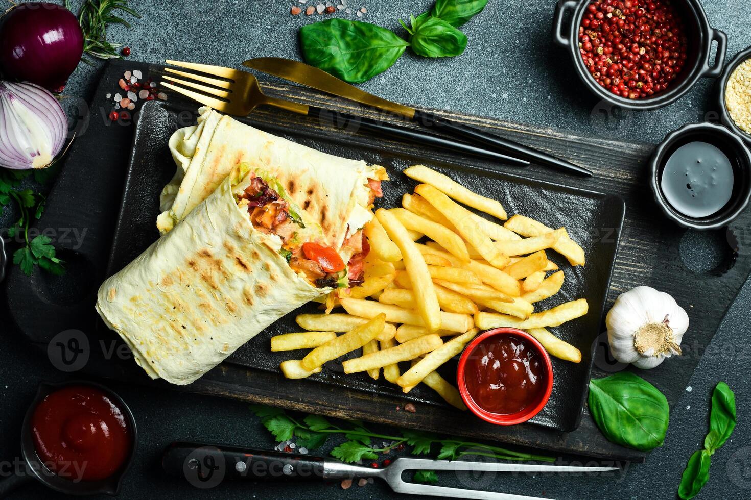 Fast food burrito with sausage and vegetables and french fries with sauce on a plate. On a dark background, close-up. photo