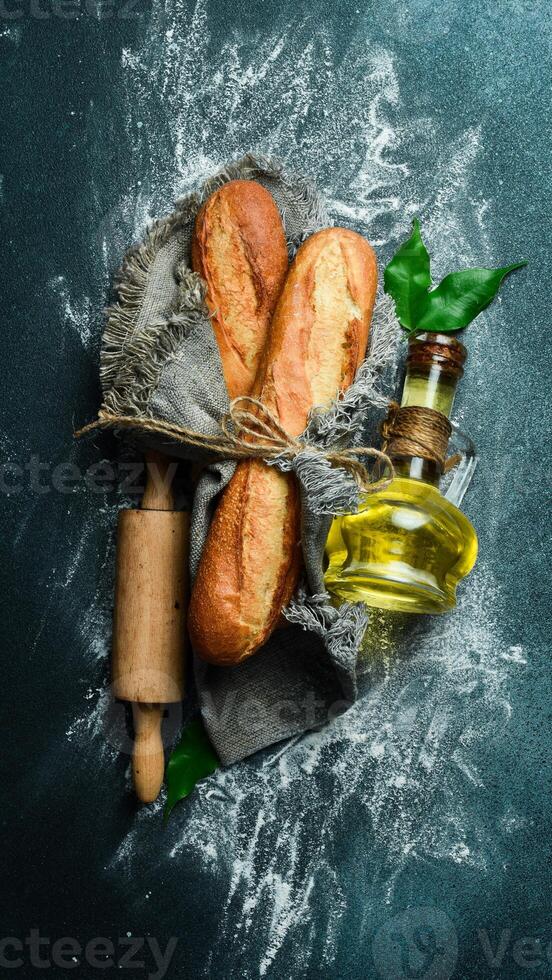 Fresh crispy baguette, a jar of oil and a rolling pin on a dark background. Free space for text. photo