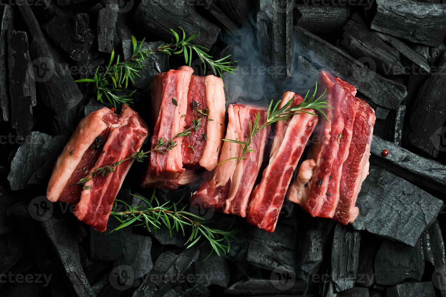 Fresh raw veal ribs with rosemary, on coals. Meat preparation, barbecue. Free space for text. photo