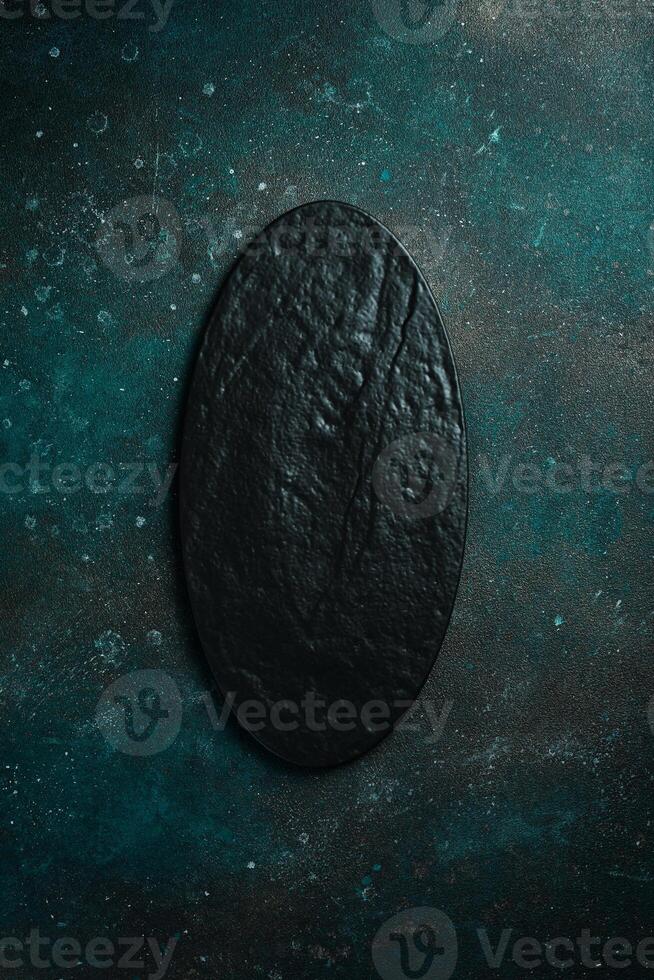 Oval slate black plate. On a dark green-turquoise background. Free space for text. photo