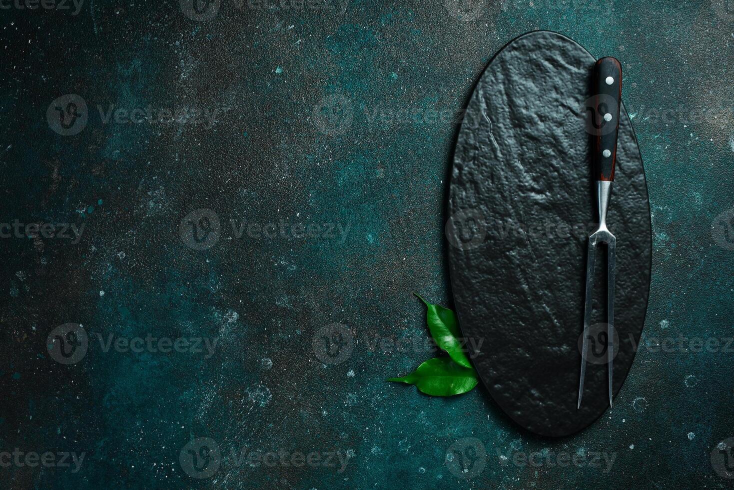 Slate plate and Metal fork for meat and steaks. On a dark green-turquoise background. Free space for text. photo