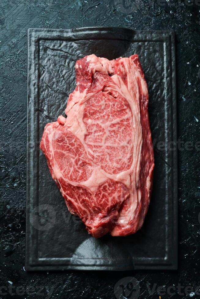 Raw marbled ribeye steak. Fresh meat and spices. Top view On a black stone background. Rustic style. photo