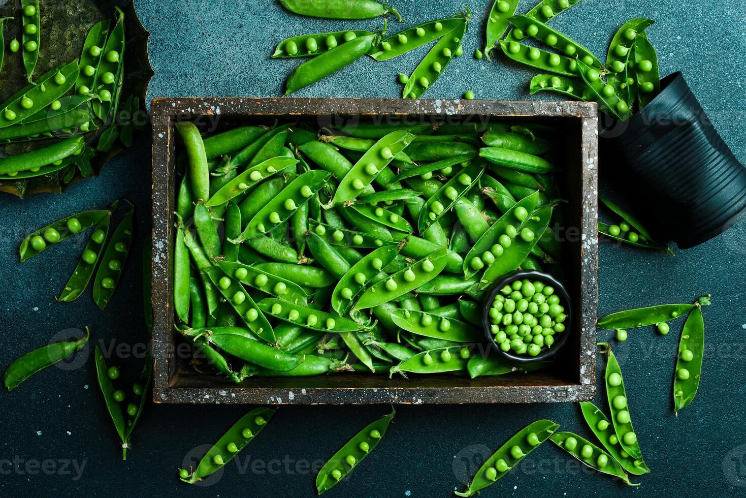 Pods of green peas with leaves in a wooden box. On a black stone background. Top view. Healthy food. photo