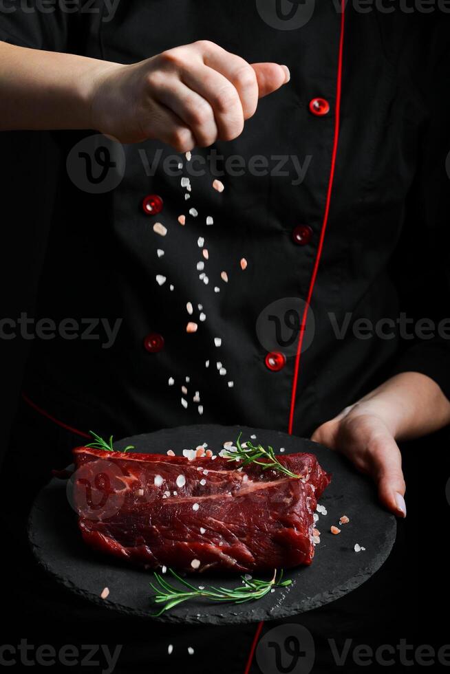 The chef is holding a plate with a piece of raw veal. Meat. On a black background. photo