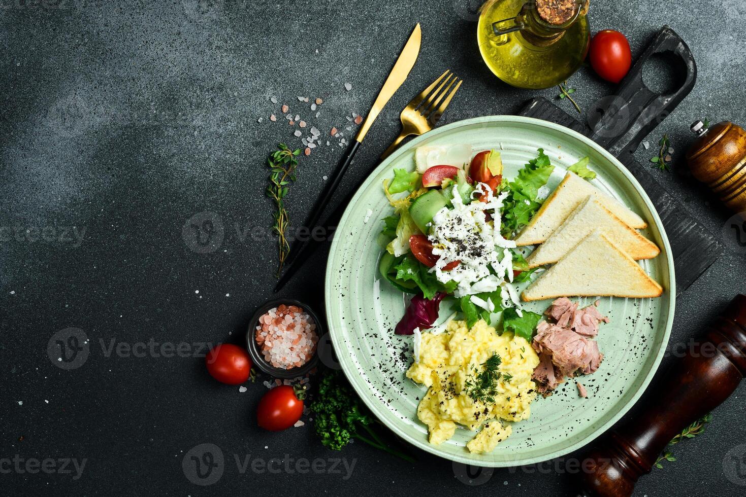 Breakfast. Plate with scrambled eggs, tuna, salad and toast bread. On a black stone background. Free space for text. photo