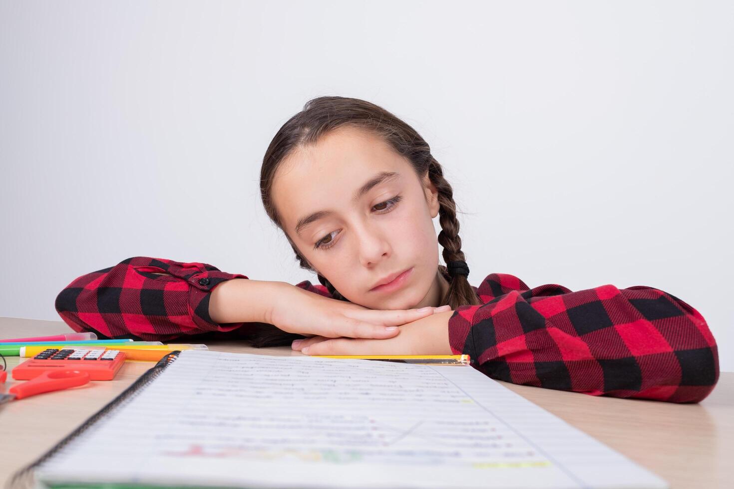 little girl with sad look looking at work notebook at school photo
