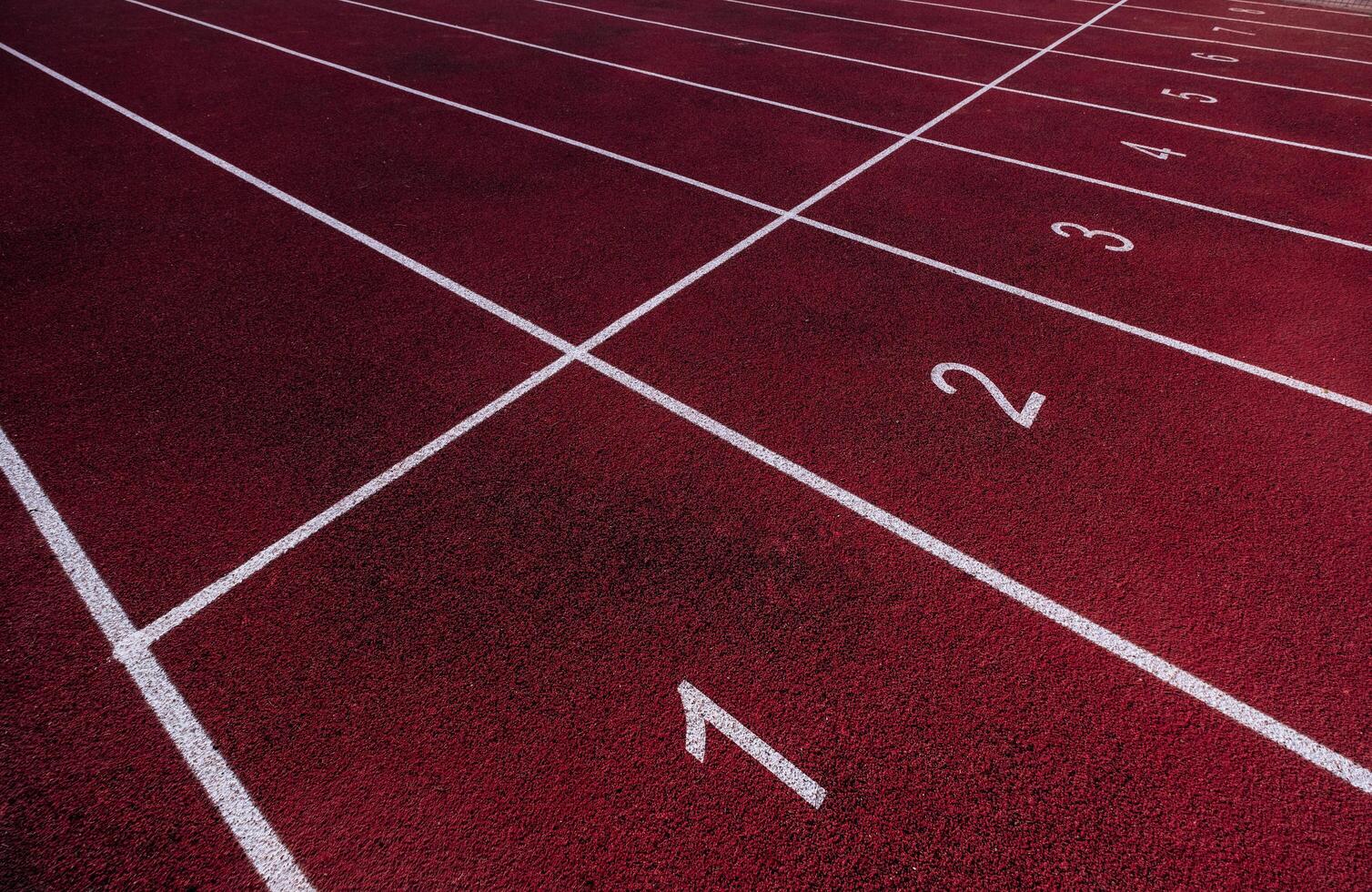 Perspective view of a red running track with white lane numbers and markings, ready for a race photo