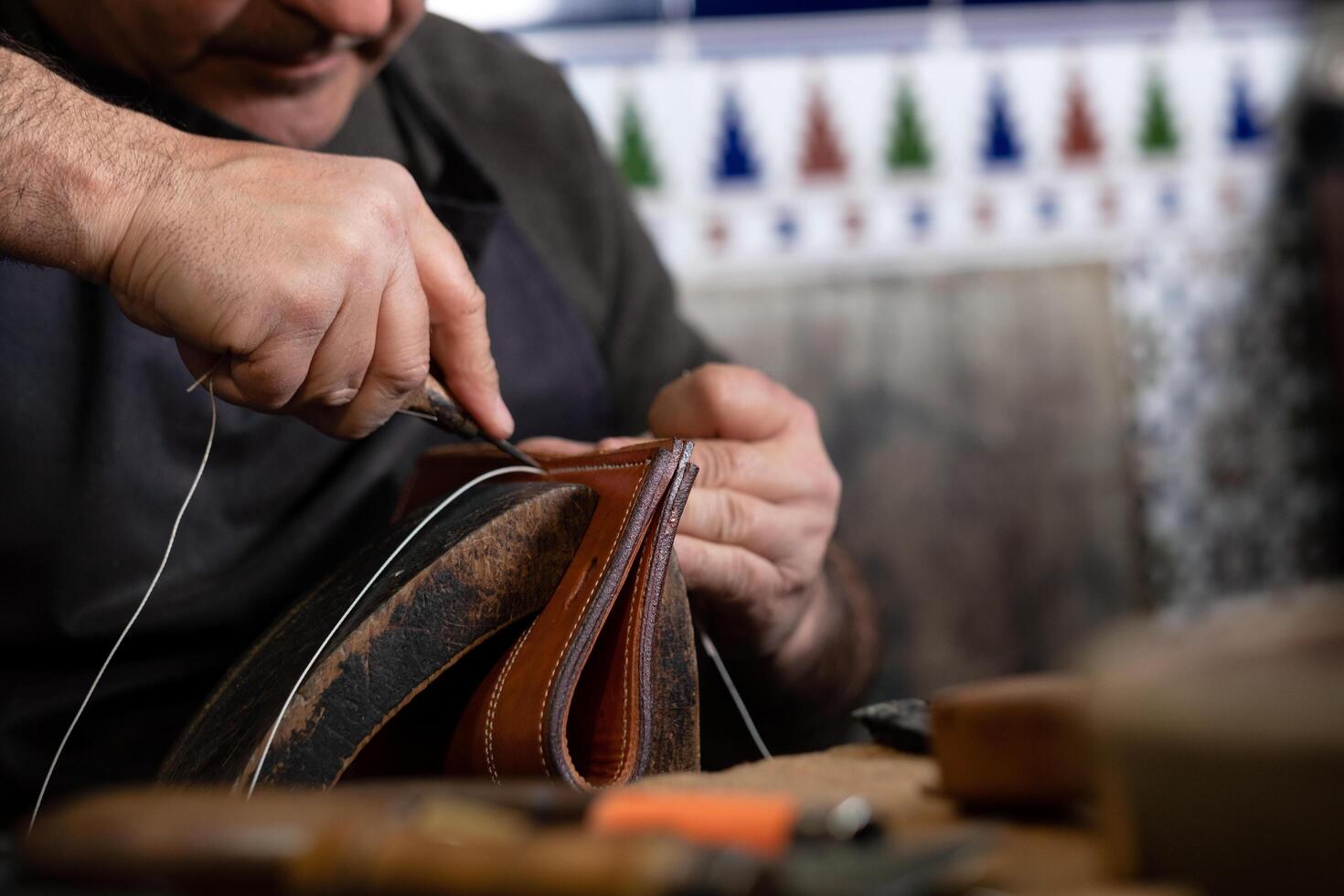 craftsman sewing piece of leather with special needle in a workshop photo