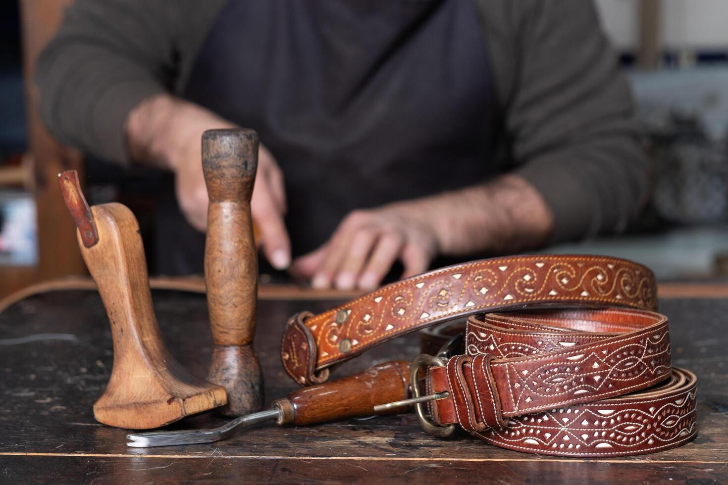 cuero cinturones con cuero herramientas en mesa y artesano trabajando detrás foto