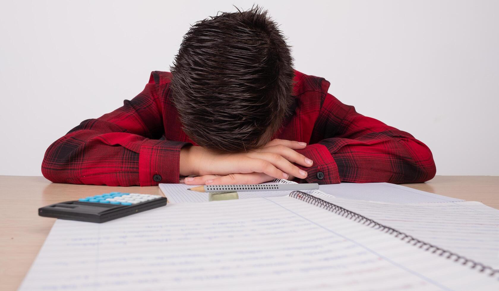 sad boy with hands on his head at the table at school photo