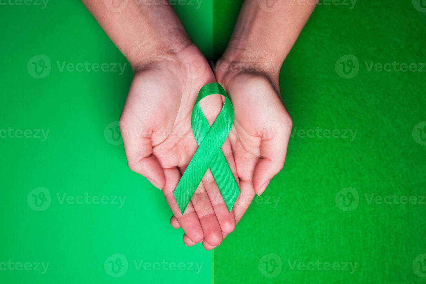 Jade tape in support of patients with hepatitis B and hepatocellular carcinoma. Green ribbon on female hands on grass background photo