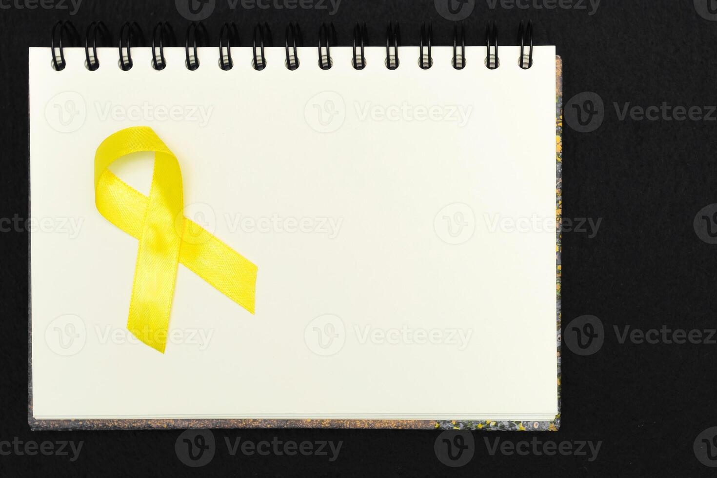 Golden ribbon for children as a symbol of childhood cancer awareness on a white notepad. World Cancer Day. photo