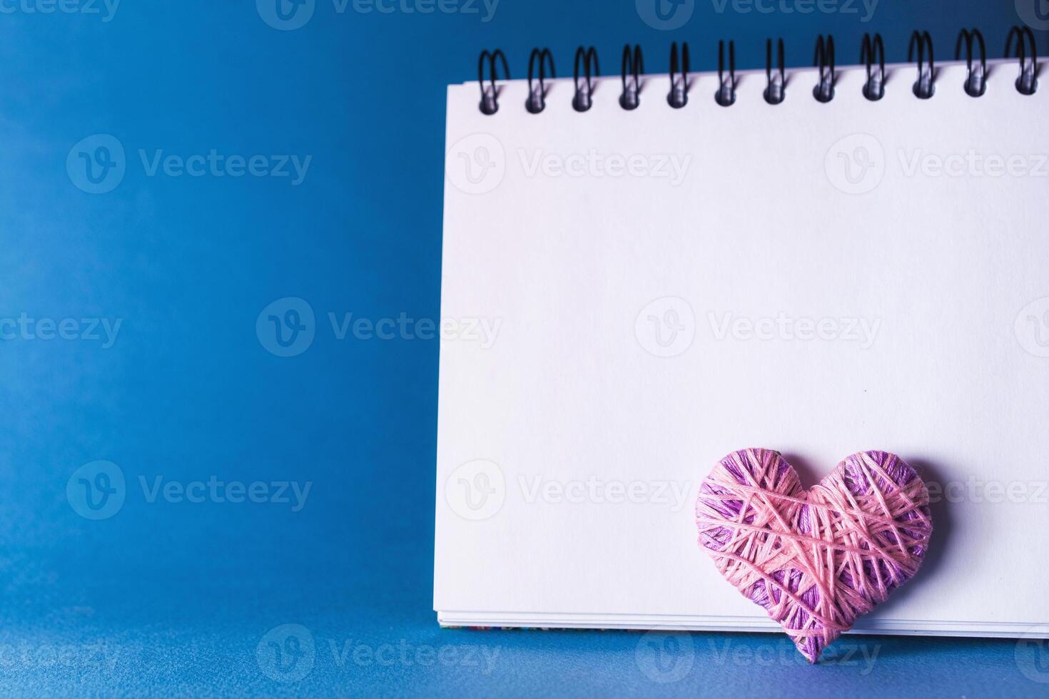 Simple blue background with a small purple red heart yn notebook. Place for text photo