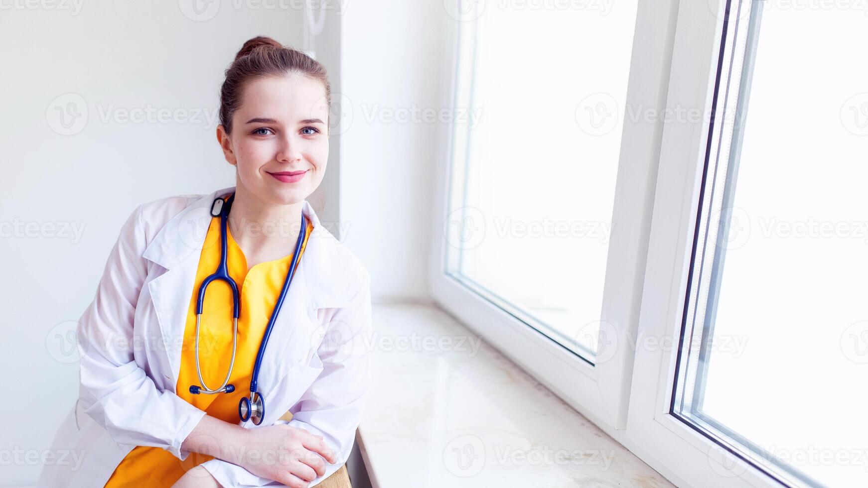 Doctor beautiful girl smiling. portrait in yellow uniform with a stethoscope near the window. Health care. background photo