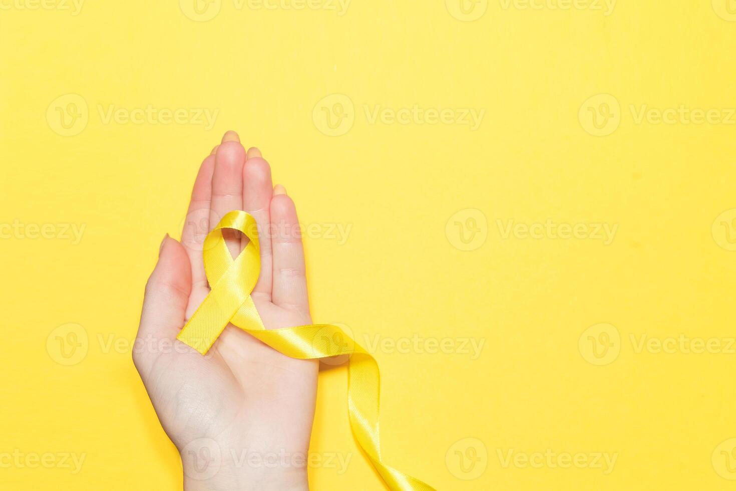 Female hand holding yellow ribbon on color background. Cancer concept photo