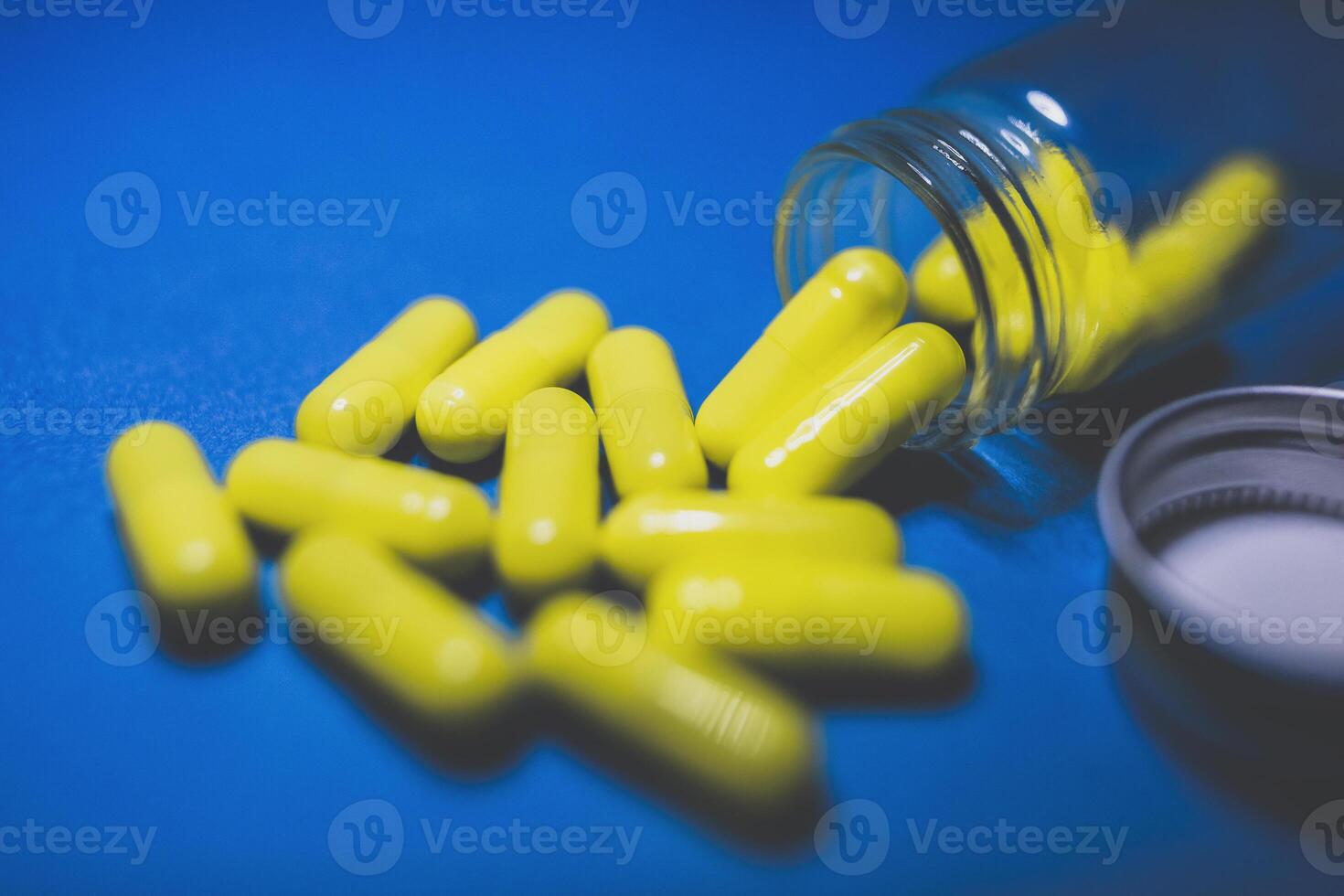 Yellow color pills on blue background and transparent glass pharmacy bottle. selective focus photo