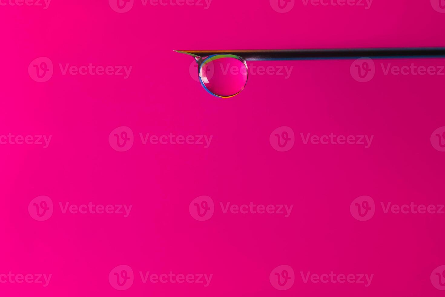 A drop of solution for injection flows along the tip of the needle of a disposable syringe. A drop of liquid medicine at the end of the needle is a pink background. The concept of plastic faces photo