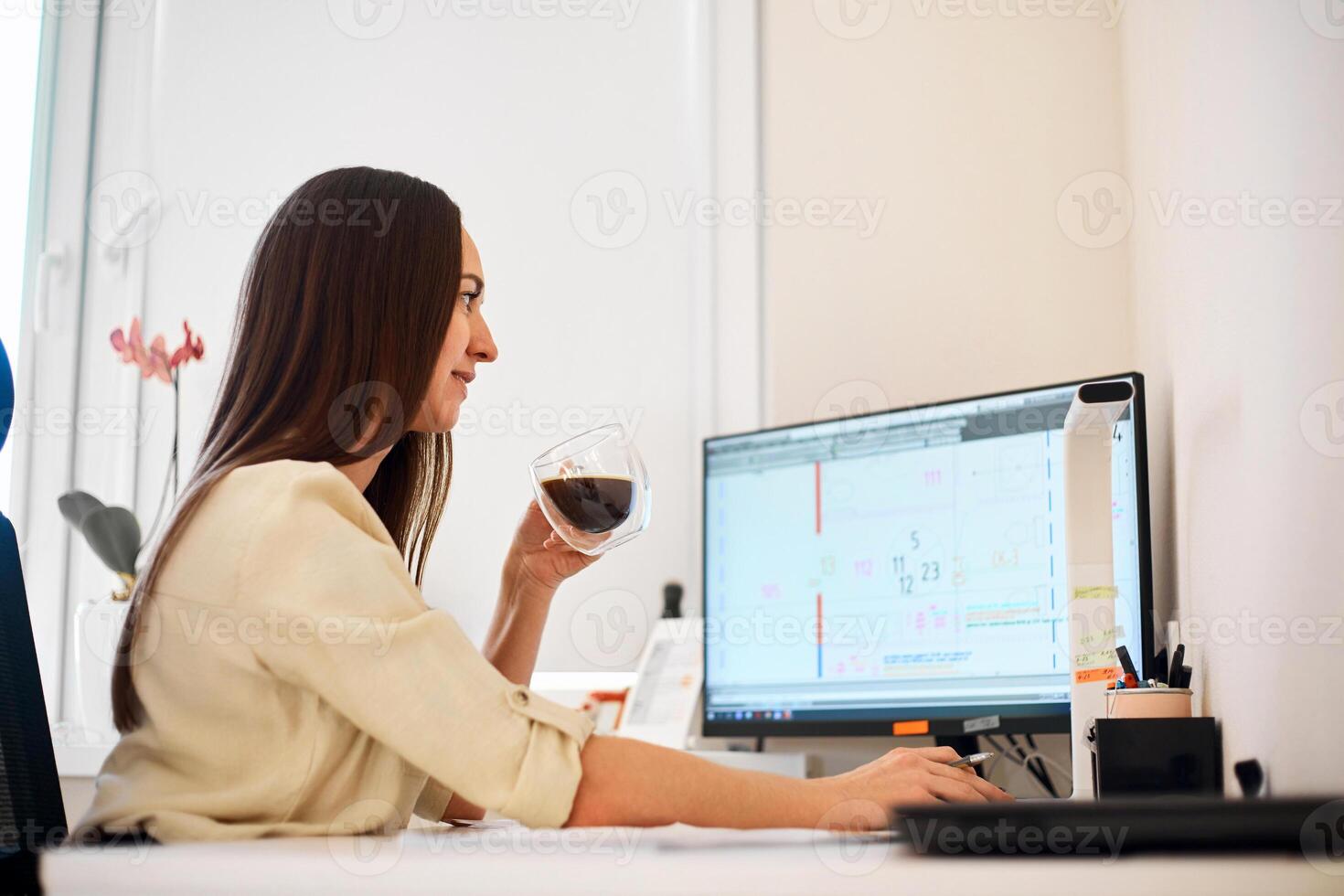 Portrait of a remote worker. A beautiful woman sits at a table in front of a computer and designs a building. Confident young lady freelancer working from home. photo