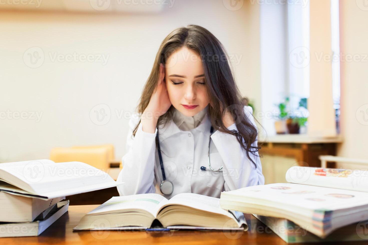 un hembra médico estudiante con un dolor de cabeza es estudiando un nuevo tema en libros de texto foto