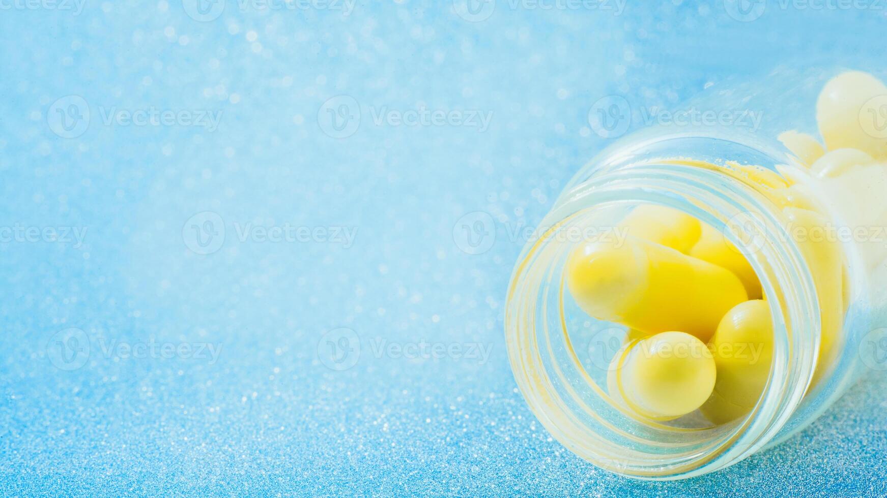 yellow capsules in a vial closeup on blue glitter, sparkles, sparkling background copy space. Global healthcare concept. Antibiotics drug resistance. Glimmer, sequins, bokeh effect. photo