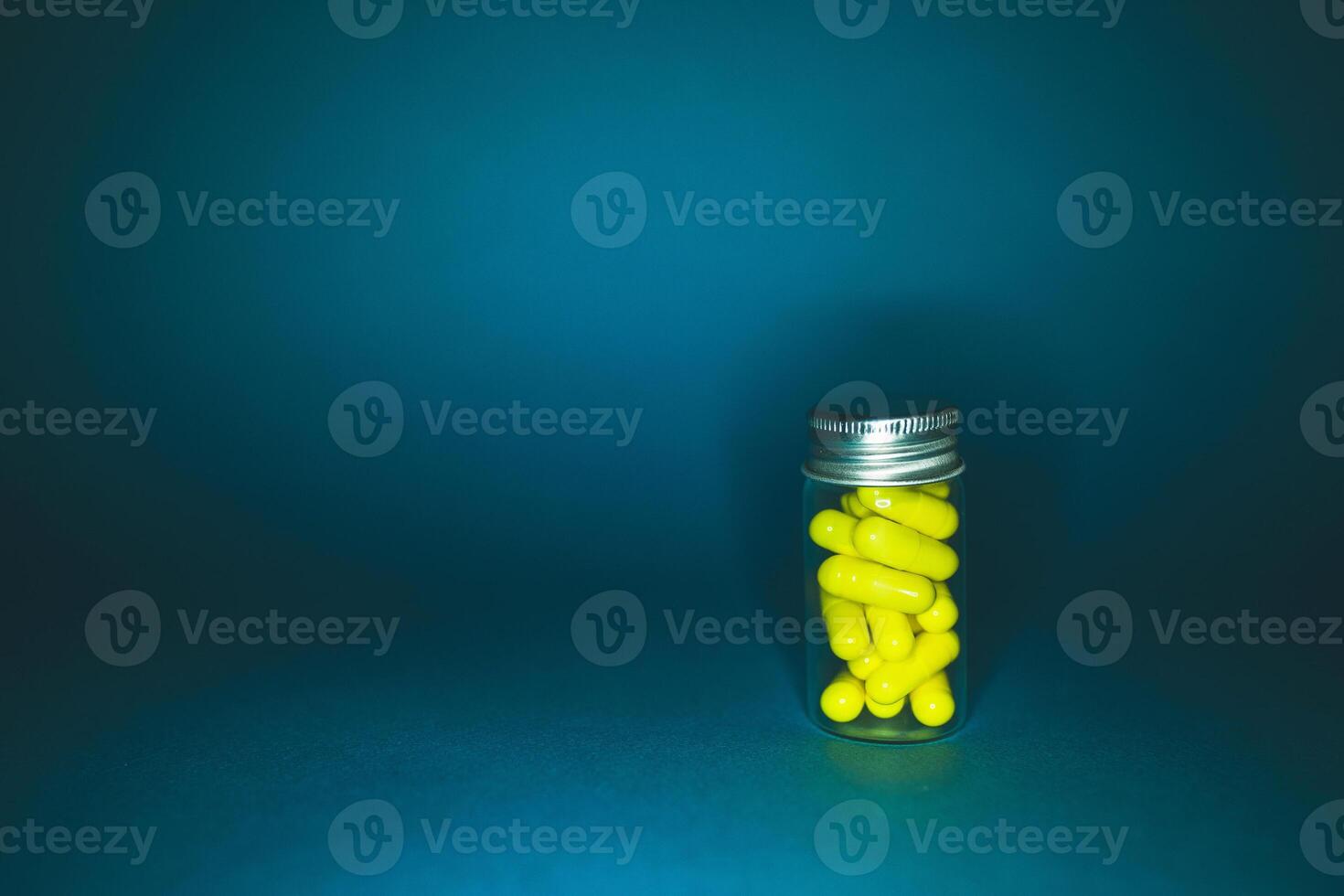 hospital drug concept. Yellow capsules in a transparent glass bottle of medium size, isolated on a dark background. Natural supplements for health. Studio lighting photo