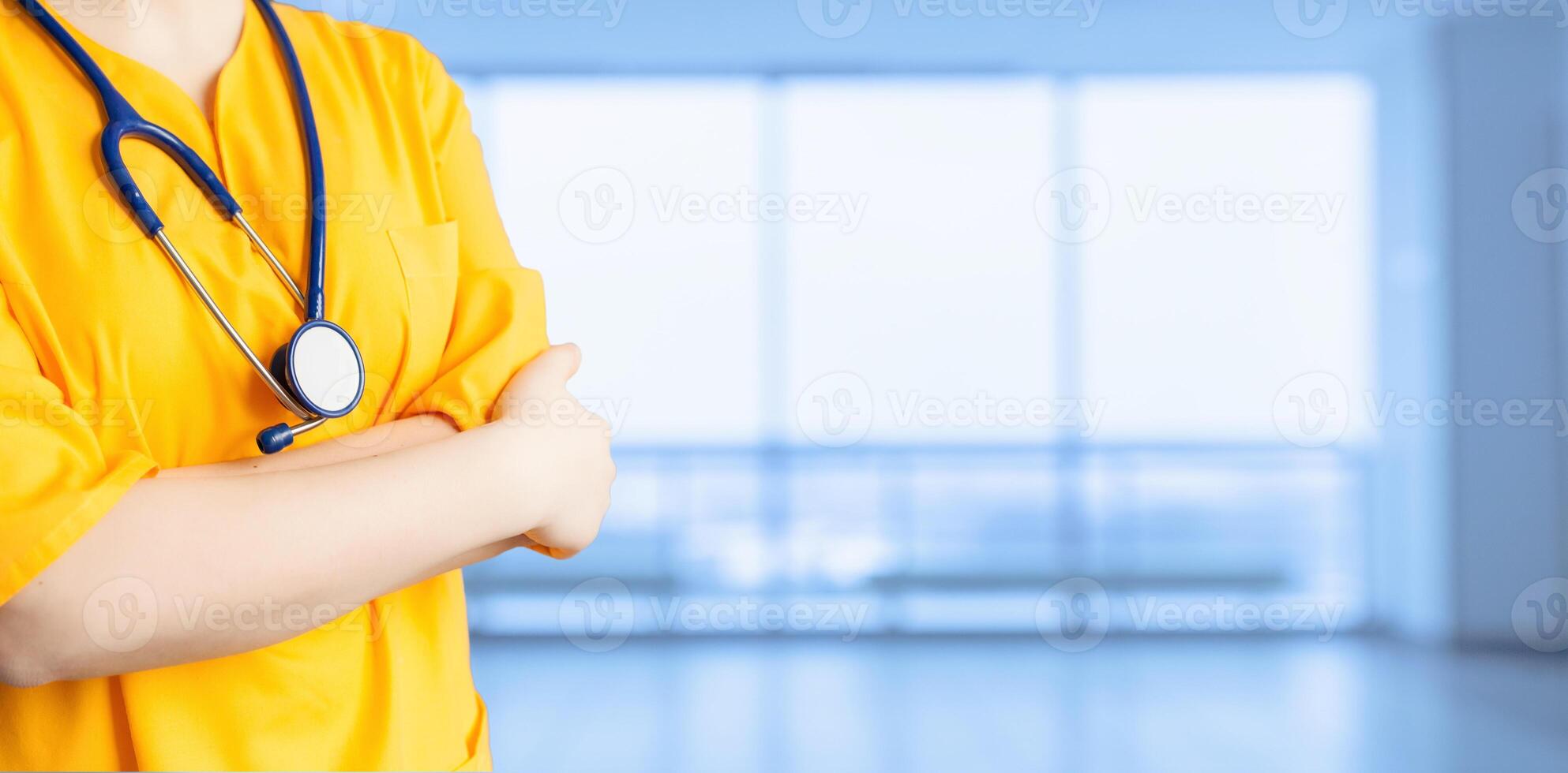 medical advertisement. Young beautiful girl in yellow coat with stethoscope and with arms crossed hospital. An impersonal wide background. photo