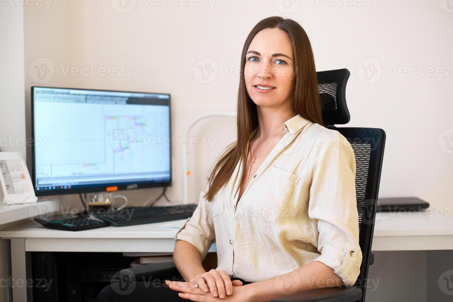 Portrait of a remote worker. A beautiful smiling brunette girl sits at a table in front of a computer and works with a layout. Confident young lady freelancer working from home. photo