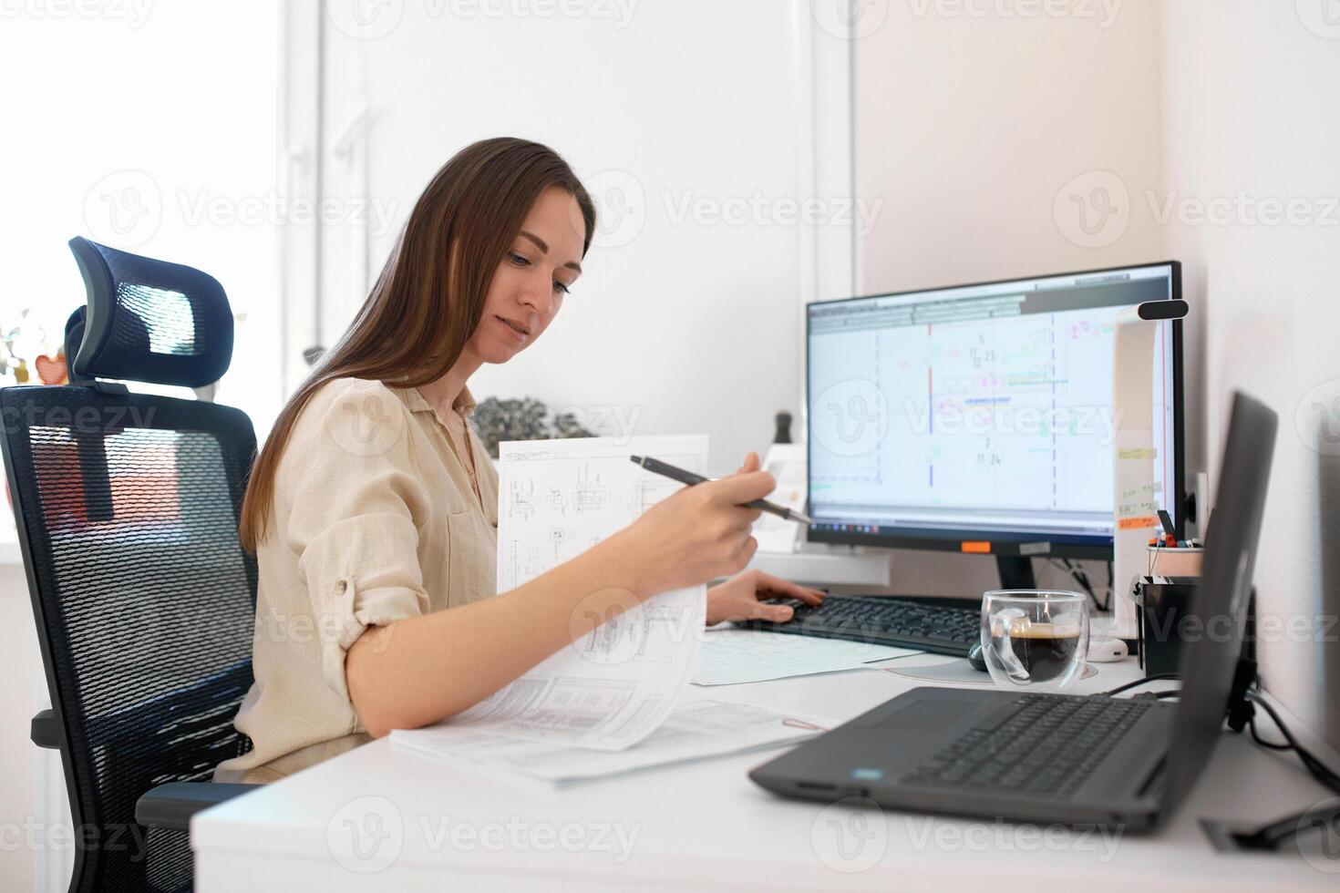 Portrait of a remote worker. An adult woman sits at a table in front of a computer and draws up a costly estimate. Confident young lady freelancer working from home. photo
