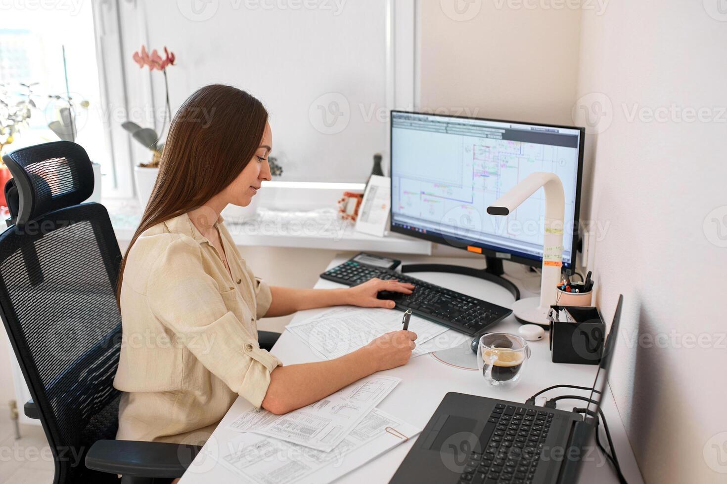 Portrait of a remote worker. An adult woman sits at a table in front of a computer and draws up a costly estimate. Confident young lady freelancer working from home. photo
