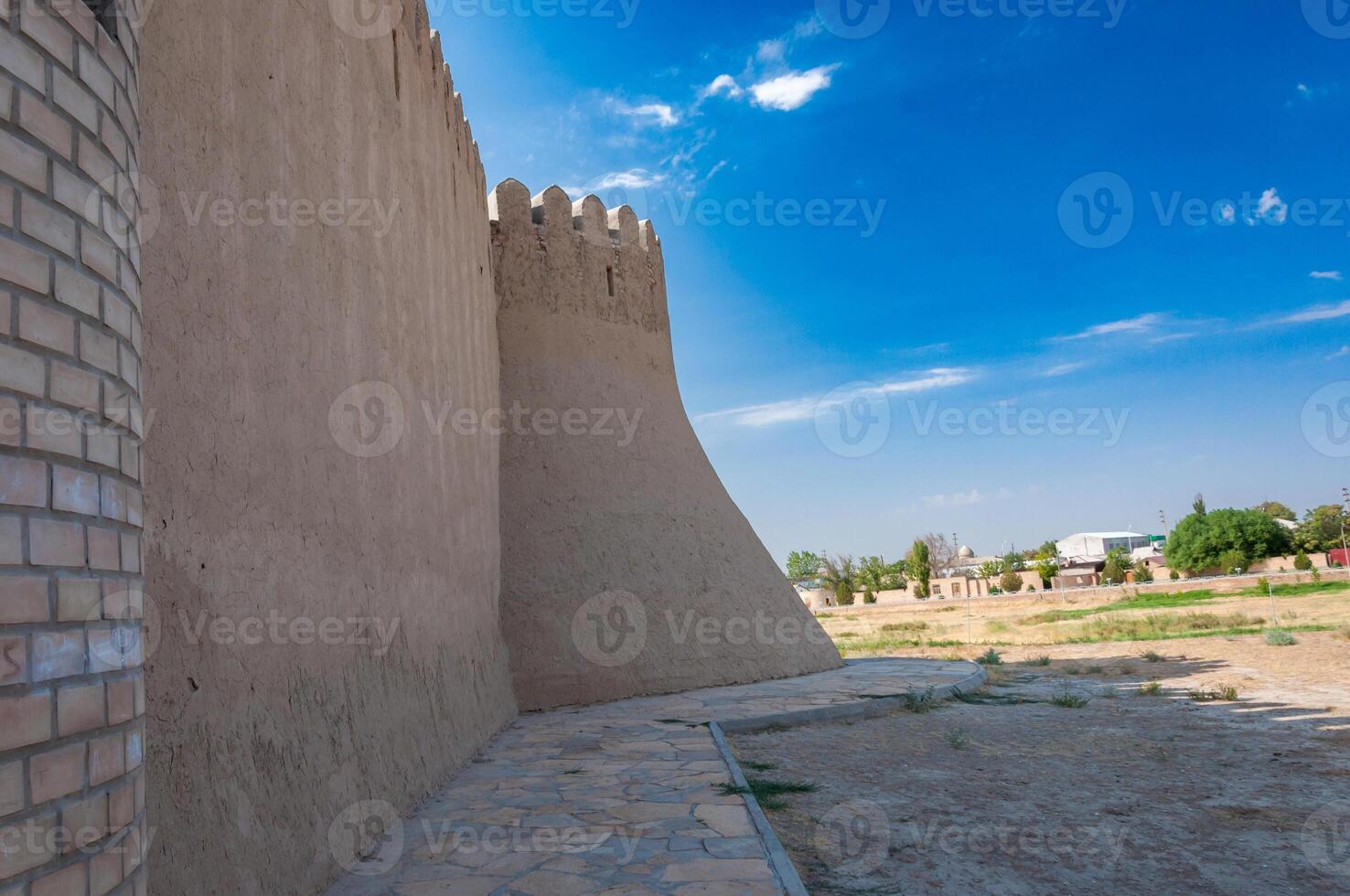 Imposing ancient fortress walls and a corner tower, featuring traditional crenellations, stretch towards the sky, juxtaposed with contemporary structures in the surrounding urban landscape. photo