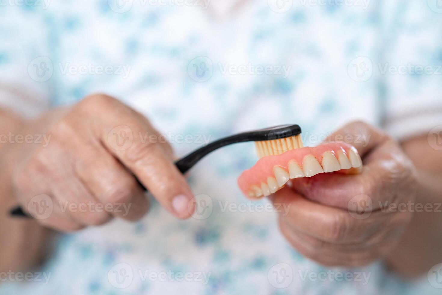 Asian elderly woman patient use toothbrush to clean partial denture of replacement teeth. photo