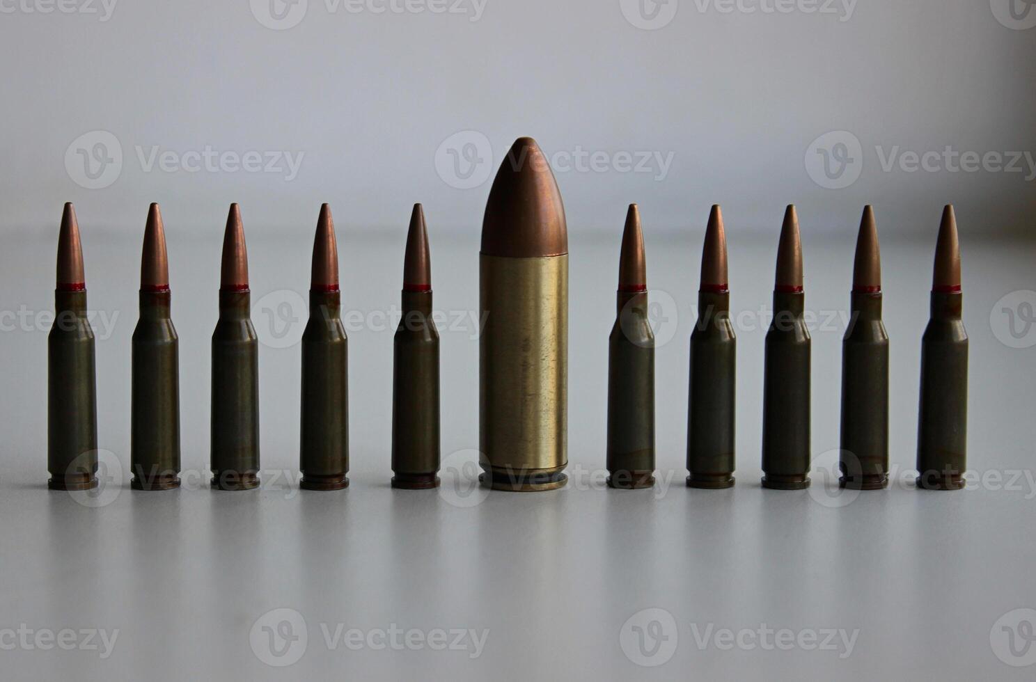 A line of identical regular caliber bullets with one huge large caliber bullet front view detailed stock photo