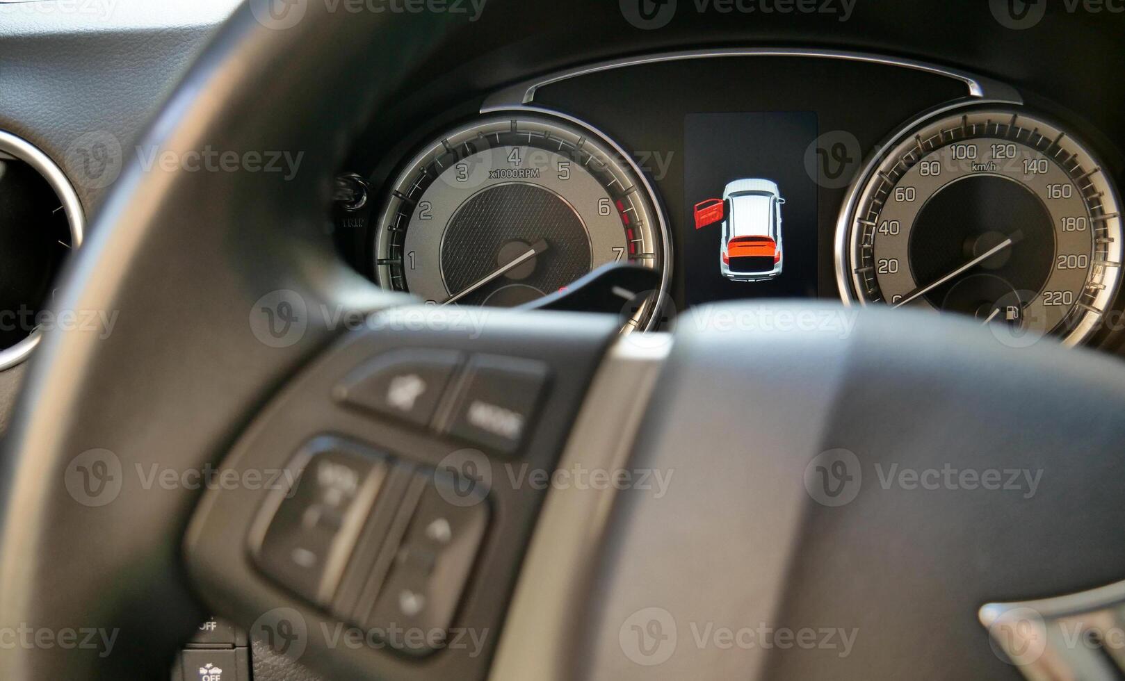 Car dashboard with illuminated open door icon behind defocused steering wheel photo