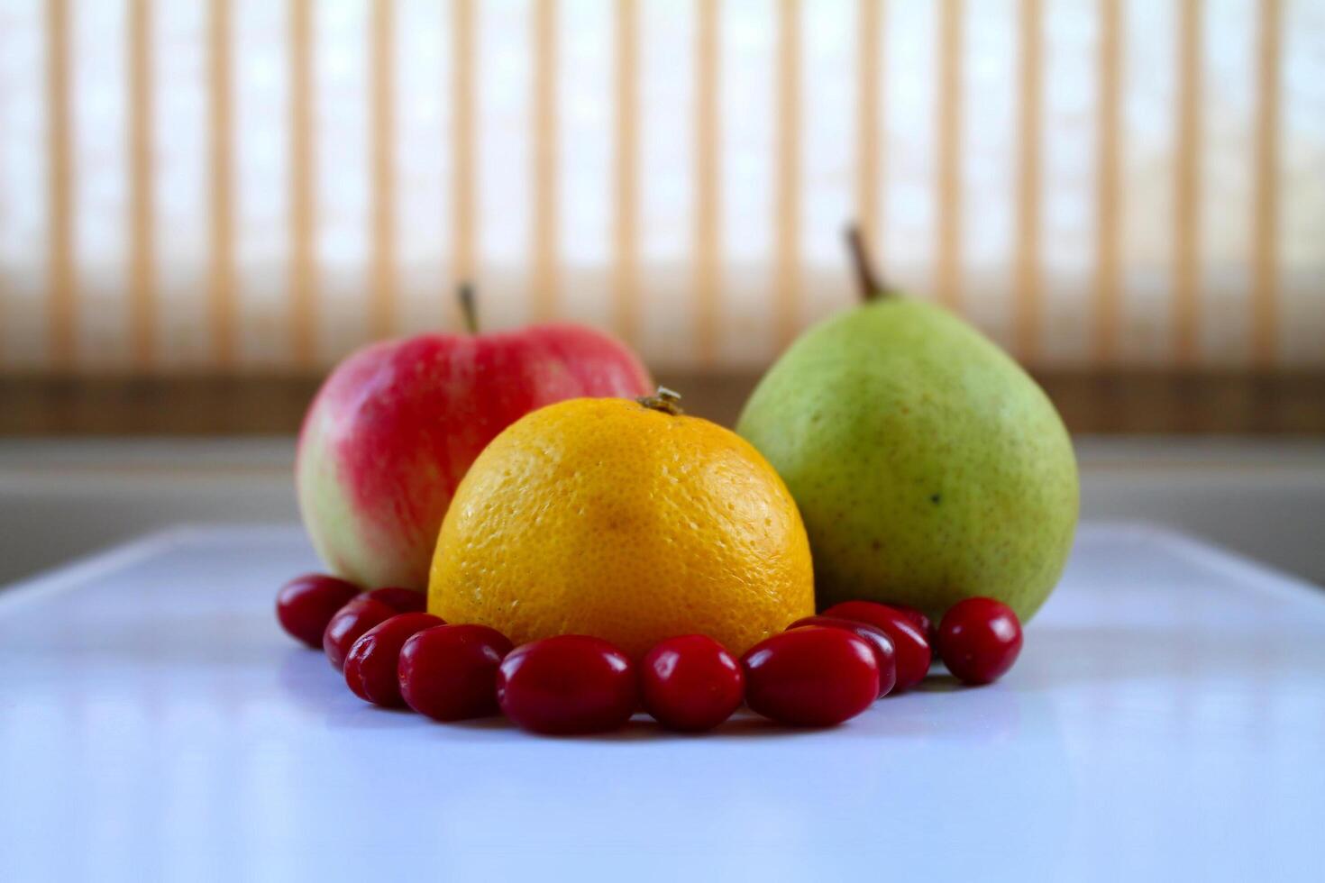 Vitamin still life. Orange, apple, pear and dogwood berries on white tray at kitchen table photo