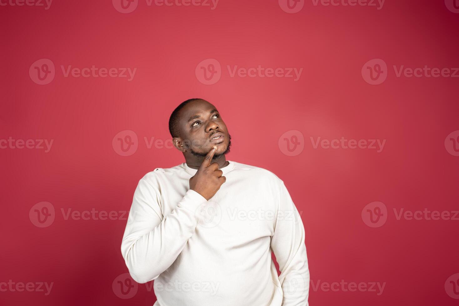 Young African American man thinking and looking up, on red background photo