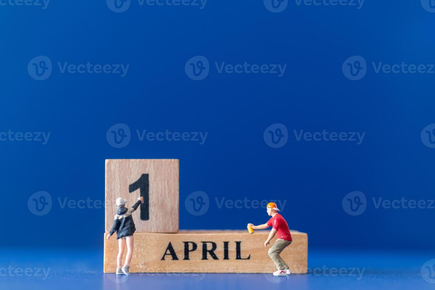 Miniature people painting a wooden block on April 1st photo