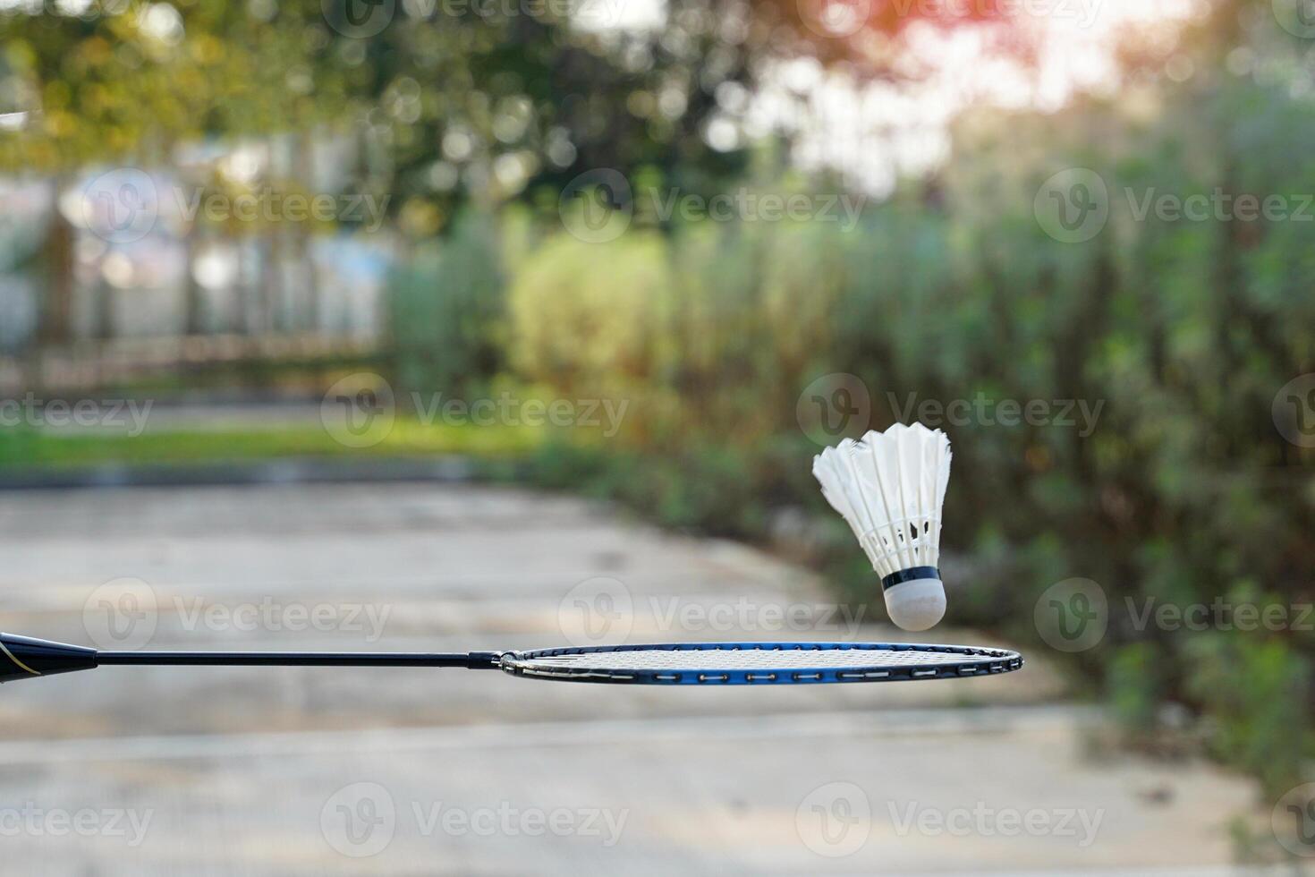 Hand holding a badminton racket to catch a falling white shuttlecock. Concept, playing badminton outdoors, free fall, gravity, sports, recreation. photo
