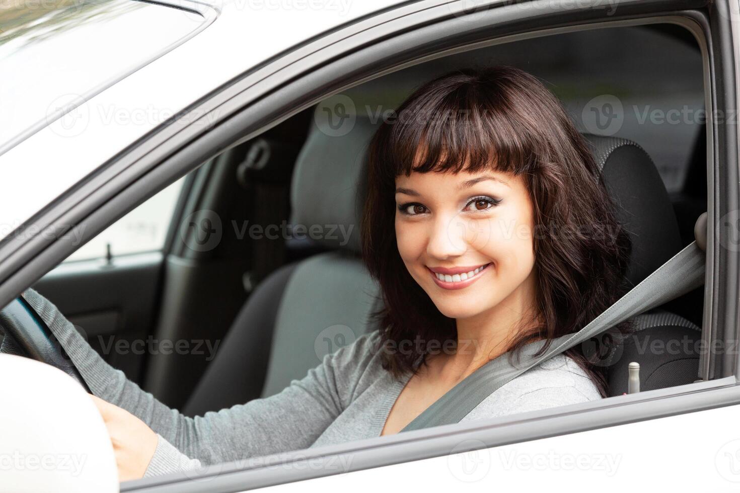 contento propietario de un nuevo coche sonriente a tú. bonito niña conductor foto