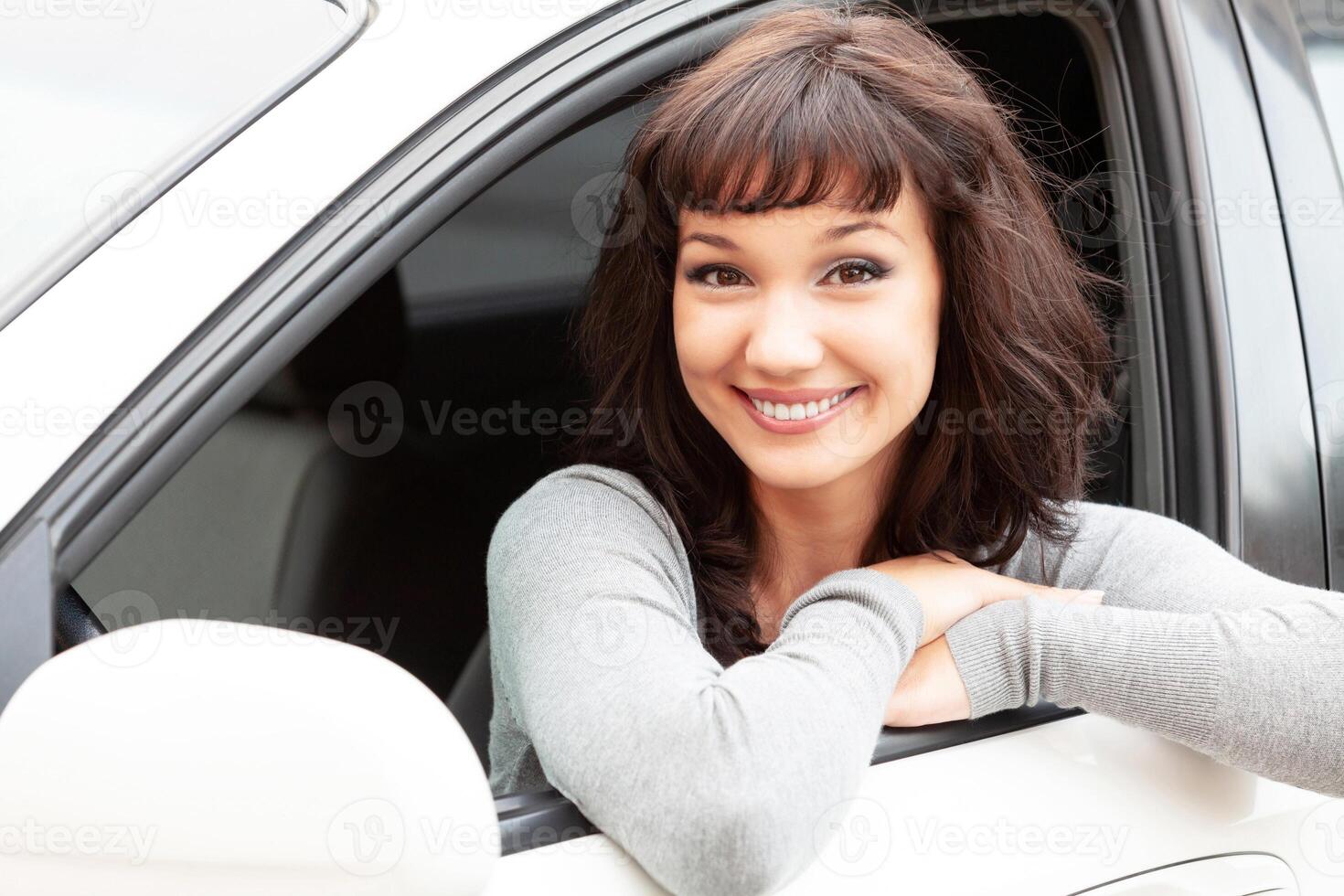 contento propietario de un nuevo coche sonriente a tú. bonito niña conductor foto