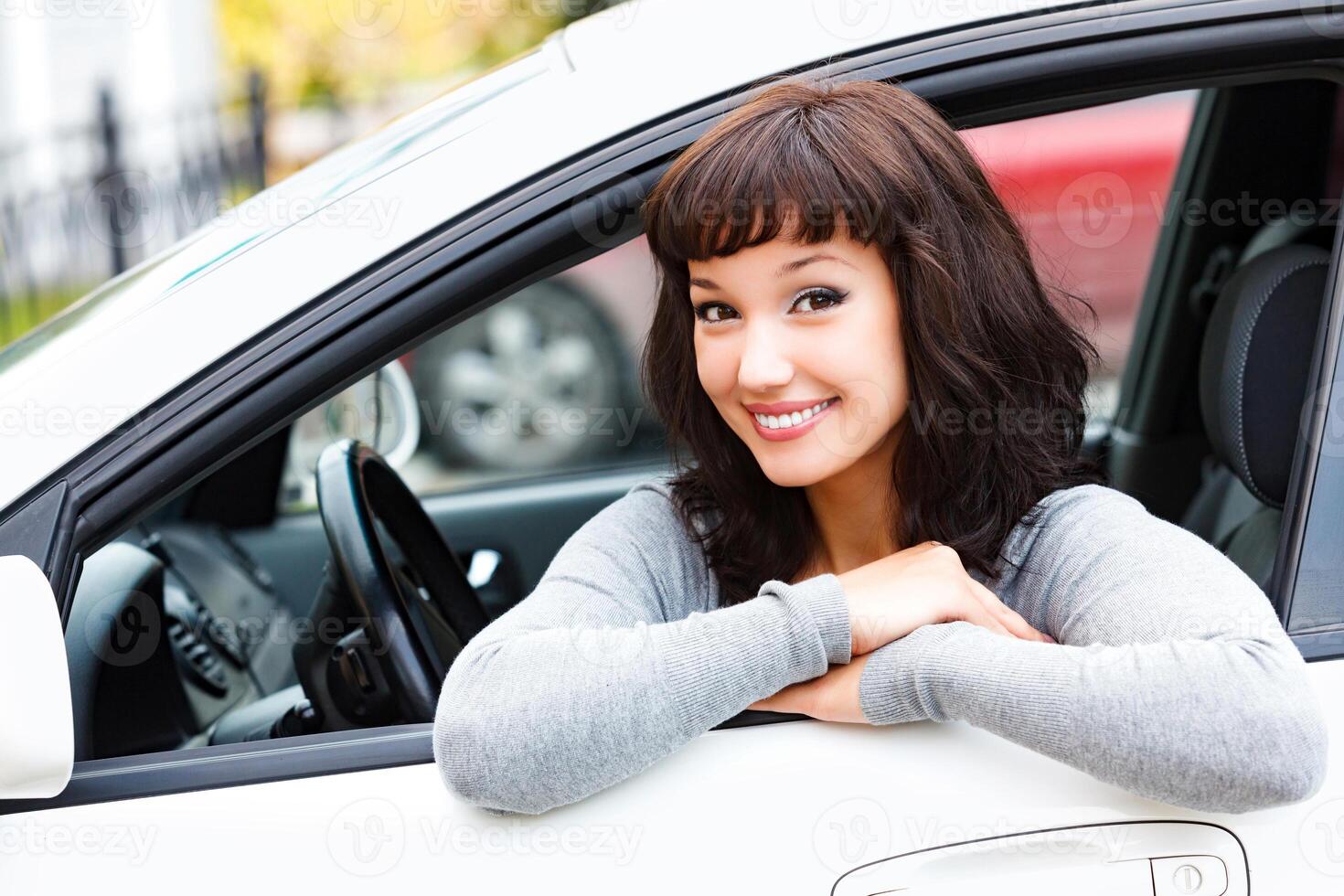 bonito mujer conductor sonriente a usted desde el blanco coche foto