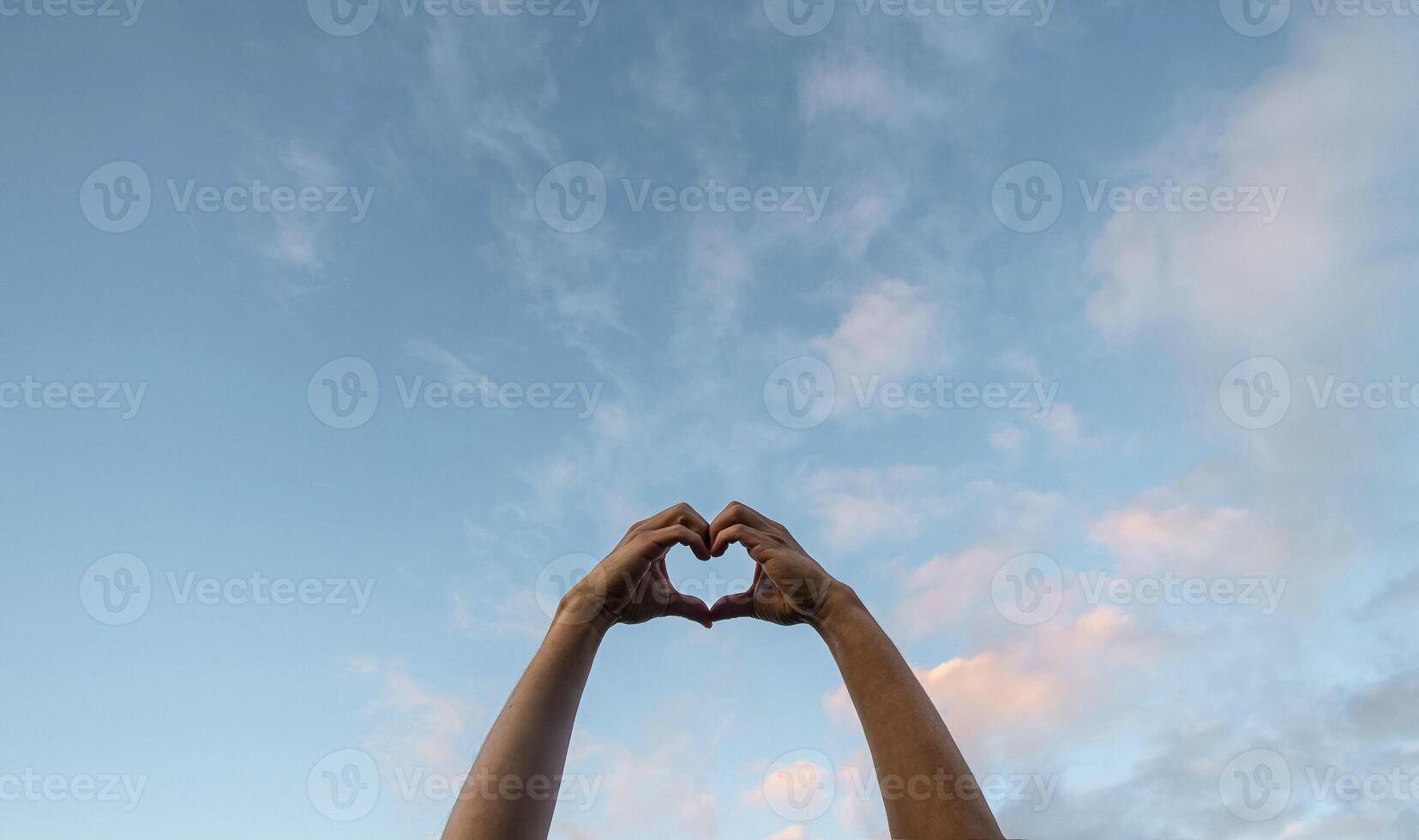 Heart shaped hands in front of a sunset photo