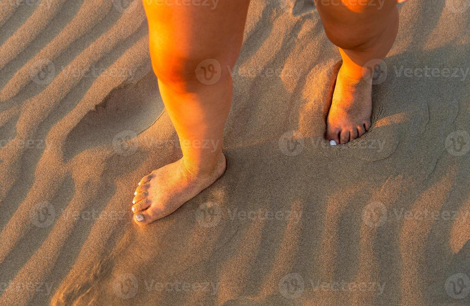 Feet of a woman walking on soft beach sand and sun rays, with space for text photo