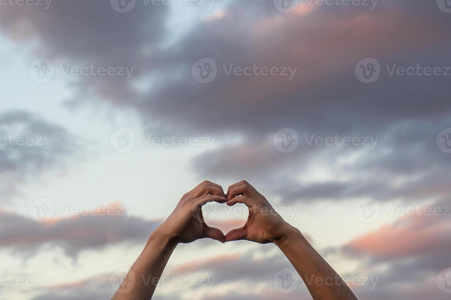 Heart shaped hands against a sunset photo