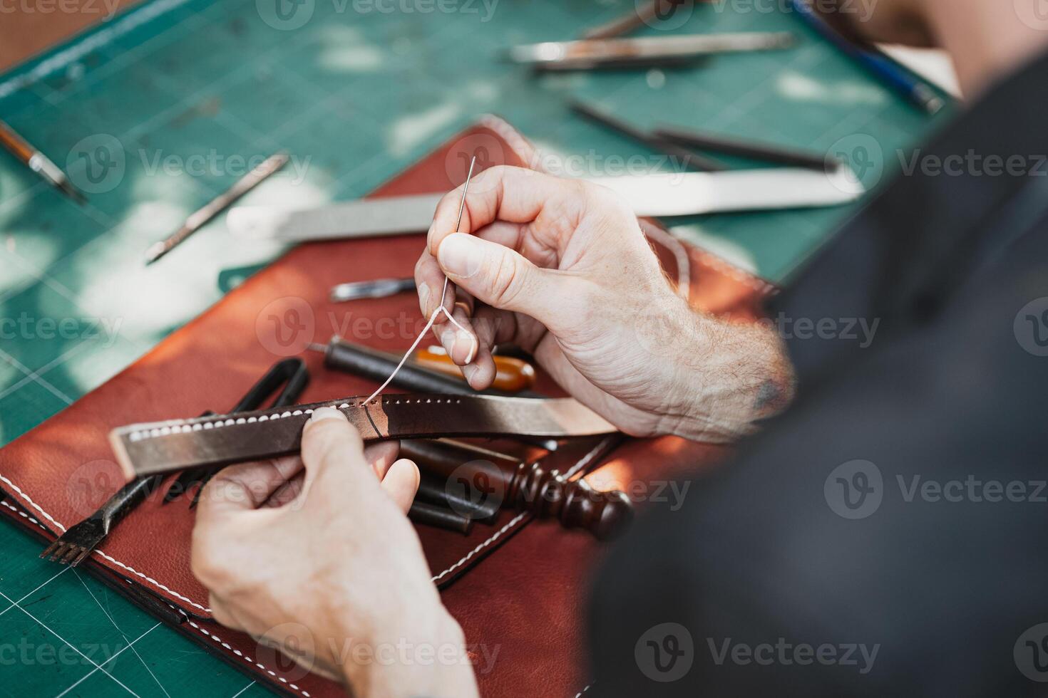 closeup hand working process leather handcraft in the leather workshop. Man holding crafting tool and working. He is sewing to make a walet. Tanner in old tannery. photo