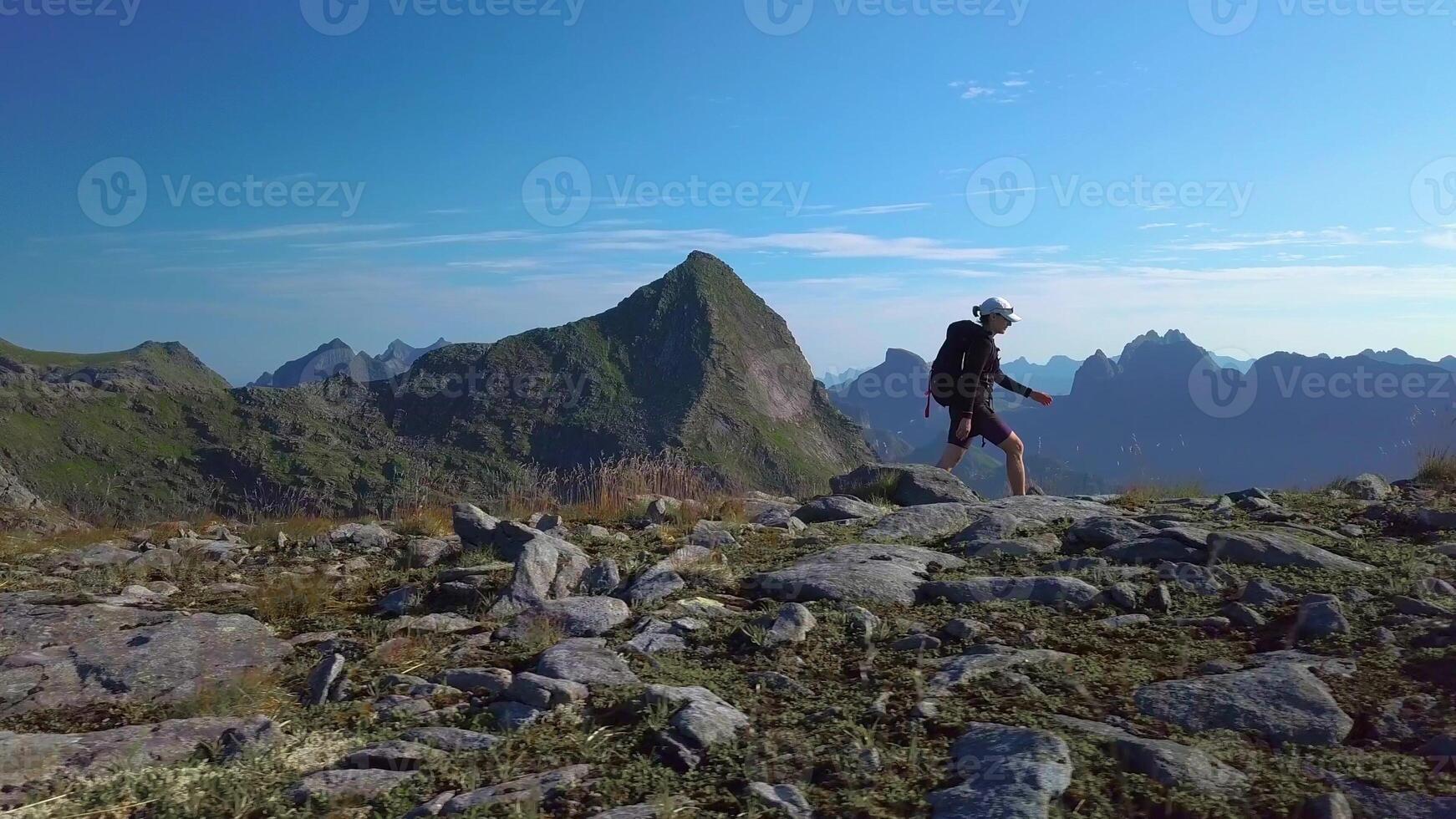 Aerial view of girl with a backpack goes on a mountain ridge. Beautiful view of the peaked tops of the Lofoten Islands. Norway 4k photo