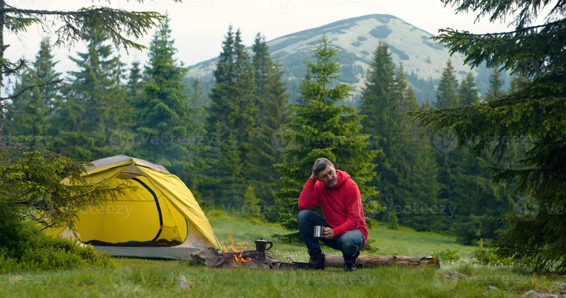 Bearded man near campfire in the forest. The camping is located in a beautiful forest lawn in the mountains. Travel concept photo