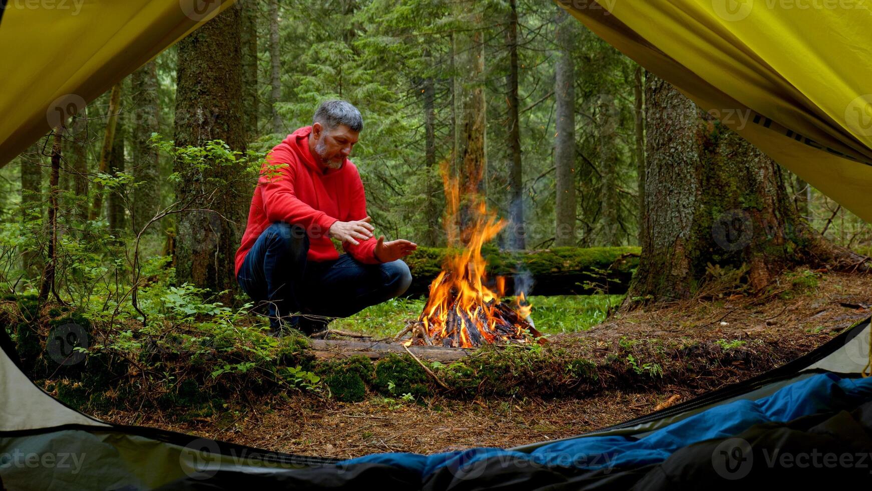 Bearded man by the fire in a beautiful forest. The camping is located in a beautiful forest lawn in the mountains. Travel concept photo