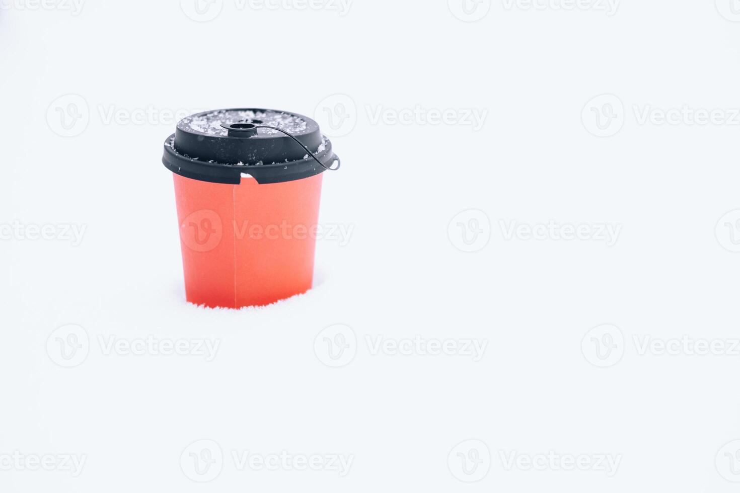 Hot coffee in a red paper cup on the snow outside during a snowfall, close-up photo