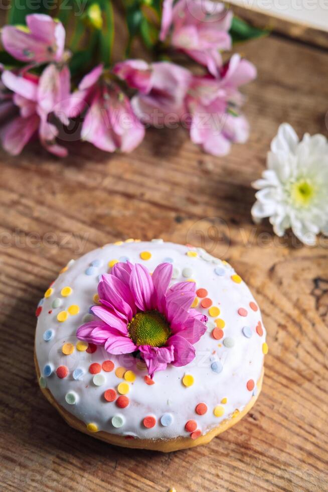 chamomile bud on top of a donut on a wooden background with a bouquet of alstroemerias. Delicate frame with pink flower photo